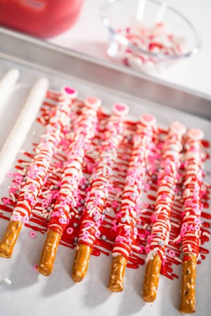 Photo for Drizzling melted chocolate over chocolate-dipped pretzels rods and decorating with sprinkles to make chocolate-covered pretzel rods for Valentine's Day. - Royalty Free Image