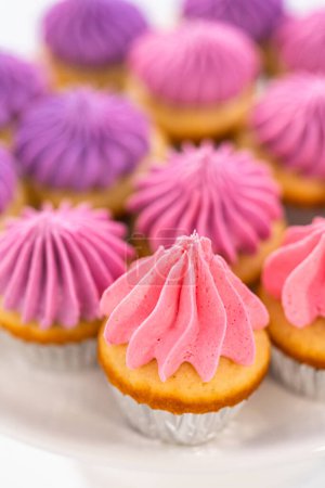 Photo for Freshly baked mini vanilla cupcakes with ombre pink buttercream frosting on a white cake stand. - Royalty Free Image