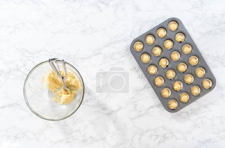 Téléchargez les photos : Flat lay. Scooping cupcake batter with dough scoop into a baking cupcake pan with liners to bake mini vanilla cupcakes with ombre pink buttercream frosting. - en image libre de droit