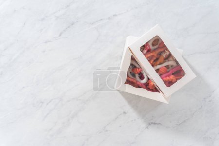 Téléchargez les photos : Pose plate. Emballage bretzel gourmet recouvert de chocolat tord dans une boîte-cadeau en papier blanc rempli de lambeaux de papier. - en image libre de droit