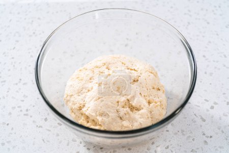Rising dough in a glass mixing bowl to bake naan dippers.
