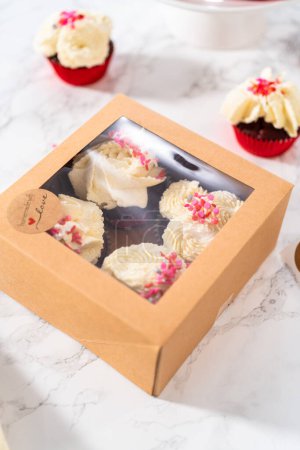 Foto de Envasado de cupcakes de terciopelo rojo recién horneados con glaseado de ganache de chocolate blanco en la caja de cupcakes. - Imagen libre de derechos