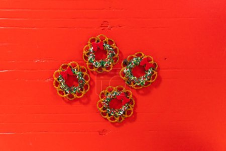 Foto de Flat lay. Chocolate pretzel Christmas wreath decorated with sprinkles and red chocolate bow on a red background. - Imagen libre de derechos