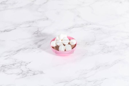 Photo for Filling in pink chocolate shells with hot chocolate mix and mini marshmallows to prepare hot chocolate bombs. - Royalty Free Image