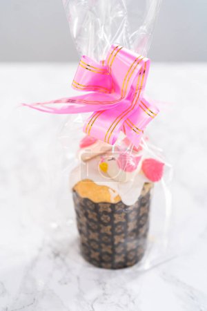Téléchargez les photos : Mini koulich de pain de Pâques enveloppé avec glaçure au citron, décoré avec des saupoudres et des biscuits meringue en forme d'oiseau comme un bon cadeau. - en image libre de droit