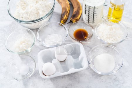 Téléchargez les photos : Ingrédients mesurés dans des bols en verre pour préparer des crêpes à la banane à la noix de coco pour le petit déjeuner. - en image libre de droit