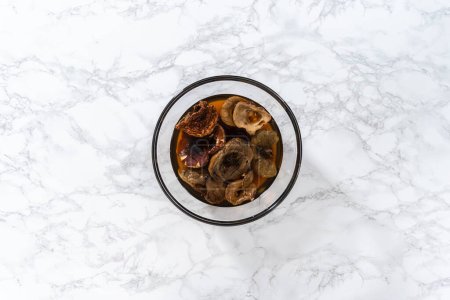 Photo for Flat lay. Soaking dehydrated wild mushrooms in a glass mixing bowl with hot water. - Royalty Free Image