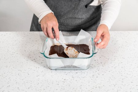 Téléchargez les photos : Verser le mélange de caramel dans le moule tapissé de papier sulfurisé pour préparer le caramel au beurre d'arachide au chocolat. - en image libre de droit