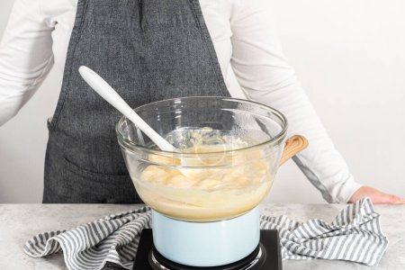 Téléchargez les photos : Faire fondre les pépites de chocolat et d'autres ingrédients dans un bol de mélange en verre sur de l'eau bouillante pour préparer le caramel au lait de poule. - en image libre de droit