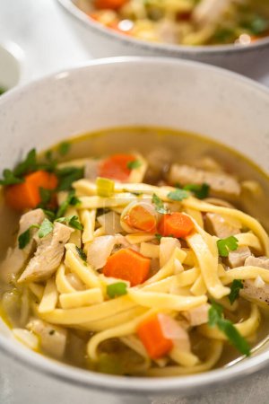 Téléchargez les photos : Servir de la soupe de nouilles de poulet avec des nouilles kluski dans des bols à soupe en céramique blanche. - en image libre de droit