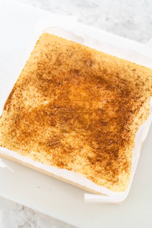 Téléchargez les photos : Enlever le caramel au lait de poule d'une poêle à gâteau au fromage carrée doublée de parchemin. - en image libre de droit