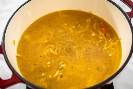 Foto de Cocinar sopa de fideos de pollo con fideos kluski en un horno holandés esmaltado. - Imagen libre de derechos