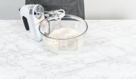 Photo for Mixing store-bought vanilla frosting in a mixing glass bowl with a hand mixer. - Royalty Free Image