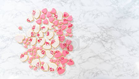 Photo for Flat lay. Decorating heart-shaped sugar cookies with pink and white royal icing for Valentines Day. - Royalty Free Image