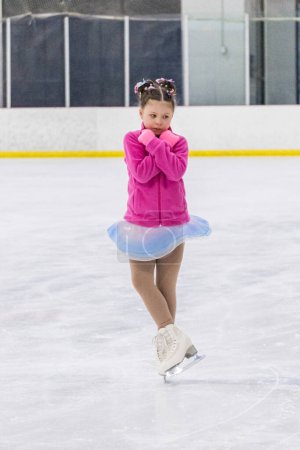 Téléchargez les photos : Petite fille pratiquant le patinage artistique sur une patinoire intérieure. - en image libre de droit