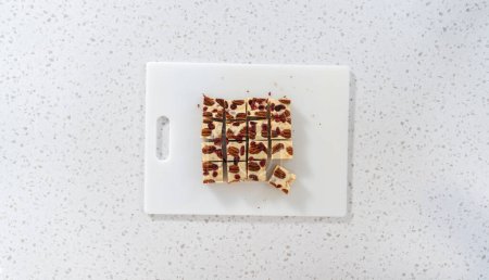 Foto de Acostado. Corte de chocolate blanco dulce de nuez de arándano en trozos pequeños en una tabla de cortar blanca. - Imagen libre de derechos
