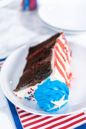 Téléchargez les photos : Tranche de gâteau au chocolat du 4 juillet décorée de glaçage à la crème au beurre rouge, blanc et bleu sur une assiette blanche. - en image libre de droit