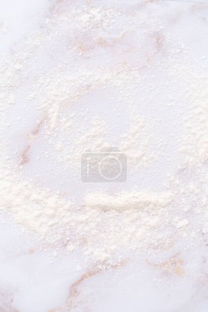 Foto de Harina blanca espolvoreada sobre la superficie de mármol rosa durante la cocción. - Imagen libre de derechos