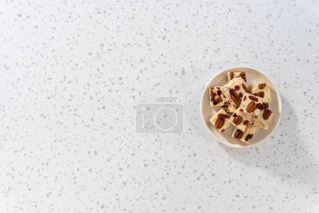 Photo for Flat lay. Homemade white chocolate cranberry pecan fudge pieces on a white ceramic plate. - Royalty Free Image