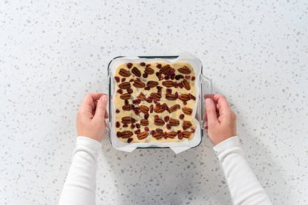 Photo for Flat lay. Removing white chocolate cranberry pecan fudge from the baking pan lined with parchment. - Royalty Free Image