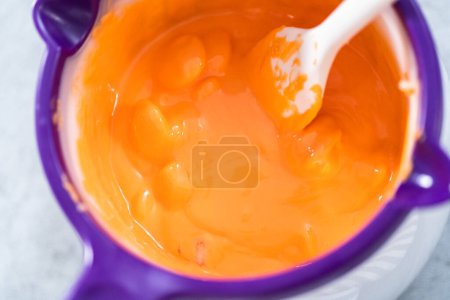 Téléchargez les photos : Fondre des pépites de chocolat de couleur dans un melting pot de bonbons pour faire des bretzels recouverts de chocolat de carotte. - en image libre de droit
