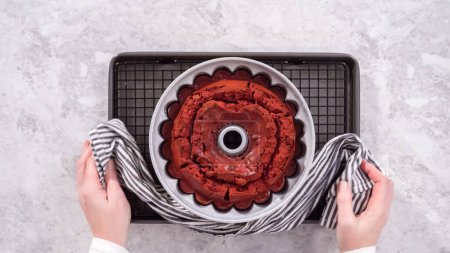 Téléchargez les photos : Pose plate. Pas à pas. Refroidissement gâteau bundt en velours rouge fraîchement cuit sur un séchoir de cuisine. - en image libre de droit