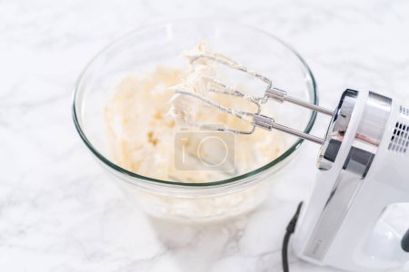 Téléchargez les photos : Mélanger les ingrédients dans un grand bol à mélanger en verre pour préparer le glaçage au fromage à la crème. - en image libre de droit