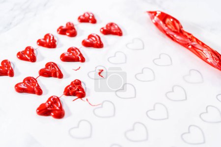 Foto de Tubería de chocolate derretido de tuberías de nuevo sobre el papel de pergamino para hacer un corazón de chocolate. - Imagen libre de derechos