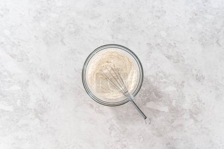 Photo for Flat lay. Mixing dry ingredients with a hand whisk in a large glass mixing bowl to bake banana cookies with chocolate drizzle. - Royalty Free Image