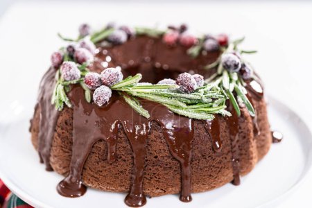 Photo for Chocolate bundt cake with chocolate frosting decorated with fresh cranberries and rosemary covered in a white sugar. - Royalty Free Image