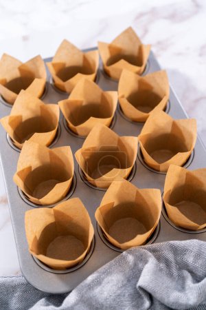 Foto de Recoger masa en la bandeja de magdalenas forrada con muffins de pergamino para hornear magdalenas sharlotka. - Imagen libre de derechos