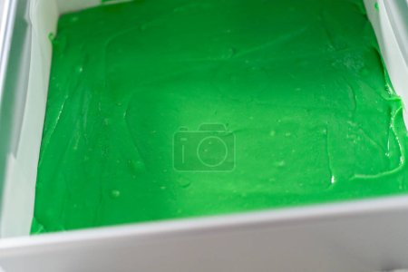 Foto de Llenado cuadrado de tarta de queso forrada con papel pergamino con mezcla de caramelo para preparar dulce verde con corazones rojos. - Imagen libre de derechos