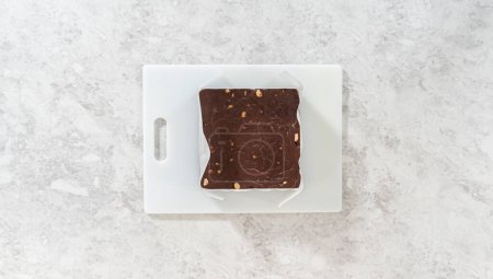Photo for Flat lay. Removing chocolate macadamia fudge from a square cheesecake pan lined with parchment. - Royalty Free Image