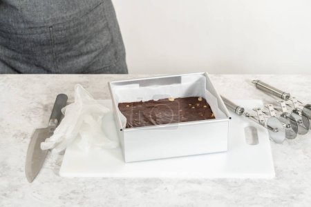 Foto de Extracción de chocolate dulce de macadamia de una sartén cuadrada de pastel de queso forrada con pergamino. - Imagen libre de derechos