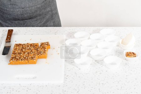 Téléchargez les photos : Coupons carrés de caramel à la citrouille faits maison en papier blanc doublures de cupcake sur un comptoir de cuisine. - en image libre de droit