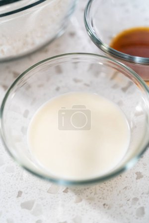 Téléchargez les photos : Ingrédients mesurés dans des bols à mélanger en verre pour faire la glaçure à la vanille pour gâteau bundt. - en image libre de droit