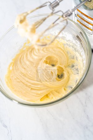 Téléchargez les photos : Mélanger les ingrédients dans un grand bol de mélange en verre pour faire la garniture de fromage à la crème pour gâteau bundt. - en image libre de droit