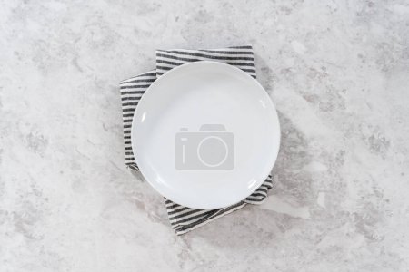 Photo for Flat lay. Empty white dinner plate with a kitchen towel on a kitchen counter. - Royalty Free Image
