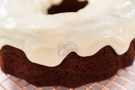 Photo for Pouring cream cheese glaze over freshly baked red velvet bundt cake. - Royalty Free Image