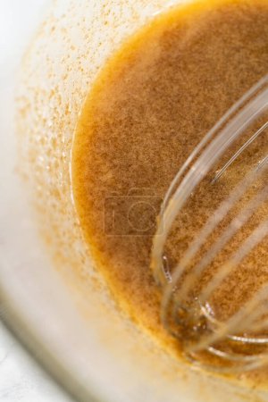 Foto de Mezclar ingredientes húmedos en un tazón de vidrio grande para hornear nuez de macadamia de chocolate blanco. - Imagen libre de derechos