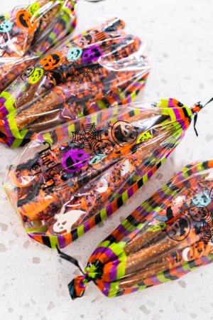 Photo for Packaging Halloween chocolate-covered pretzel rods with sprinkles into gift bags. - Royalty Free Image