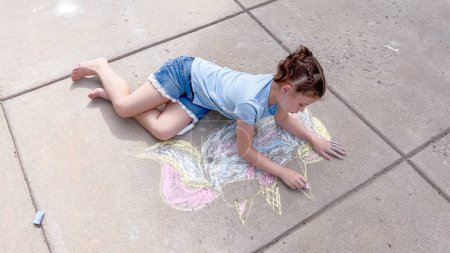 Foto de Niña dibujando tiza en un camino suburbano en un día de verano. - Imagen libre de derechos