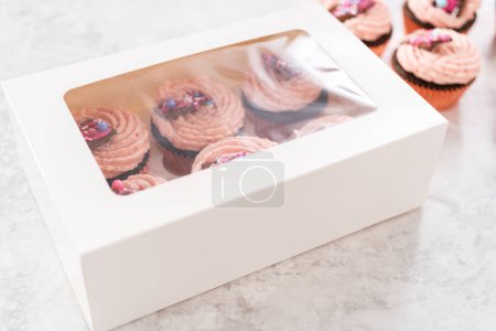 Téléchargez les photos : Emballage de cupcakes fraises au chocolat fraîchement cuits garnis de mini chocolats roses gourmands dans une boîte à cupcakes en papier blanc. - en image libre de droit