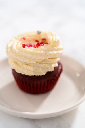Photo for Freshly baked velvet cupcakes with white chocolate ganache frosting decorated with sprinkles. - Royalty Free Image
