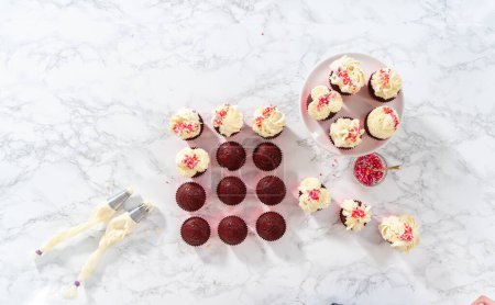 Téléchargez les photos : Pose plate. Piping glaçage ganache chocolat blanc sur le dessus de cupcakes en velours rouge et garniture de saupoudrer. - en image libre de droit