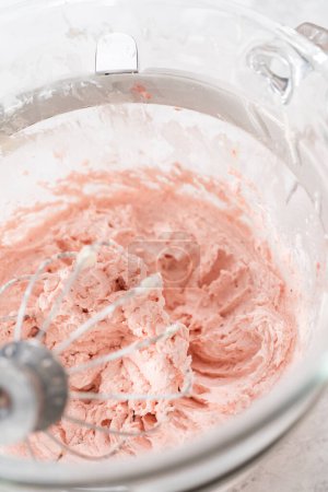 Téléchargez les photos : Fouetter le glaçage à la crème au beurre à la fraise dans un mélangeur électrique autonome muni d'un fouet. - en image libre de droit