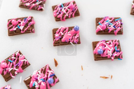 Téléchargez les photos : Arrosant chocolat rose fondu sur le dessus des mini chocolats et saupoudrer quelques saupoudres colorées sur le dessus. - en image libre de droit