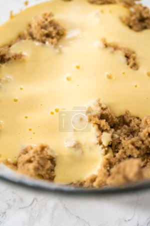 Téléchargez les photos : Mélange d'ingrédients humides dans un grand bol à mélanger en verre pour cuire des cupcakes en velours rouge avec glaçage ganache au chocolat blanc. - en image libre de droit