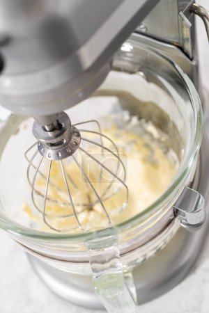 Téléchargez les photos : Fouetter le glaçage à la crème au beurre à la fraise dans un mélangeur électrique autonome muni d'un fouet. - en image libre de droit