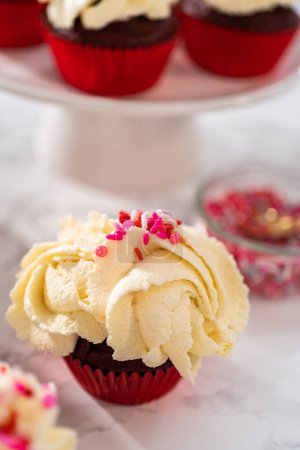 Photo for Freshly baked velvet cupcakes with white chocolate ganache frosting decorated with sprinkles. - Royalty Free Image